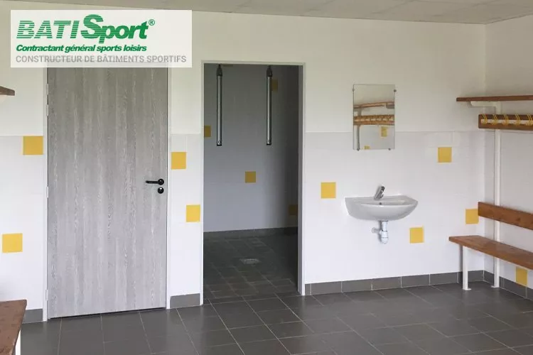 Interieur des vestiaires sportifs avec bancs et salle de douche.